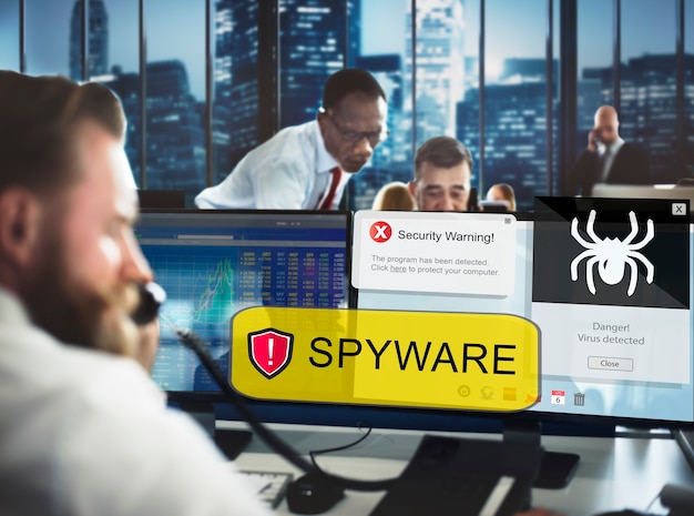 Office workers reacting to a spyware alert on a computer screen, displaying security warnings and a virus detection message.